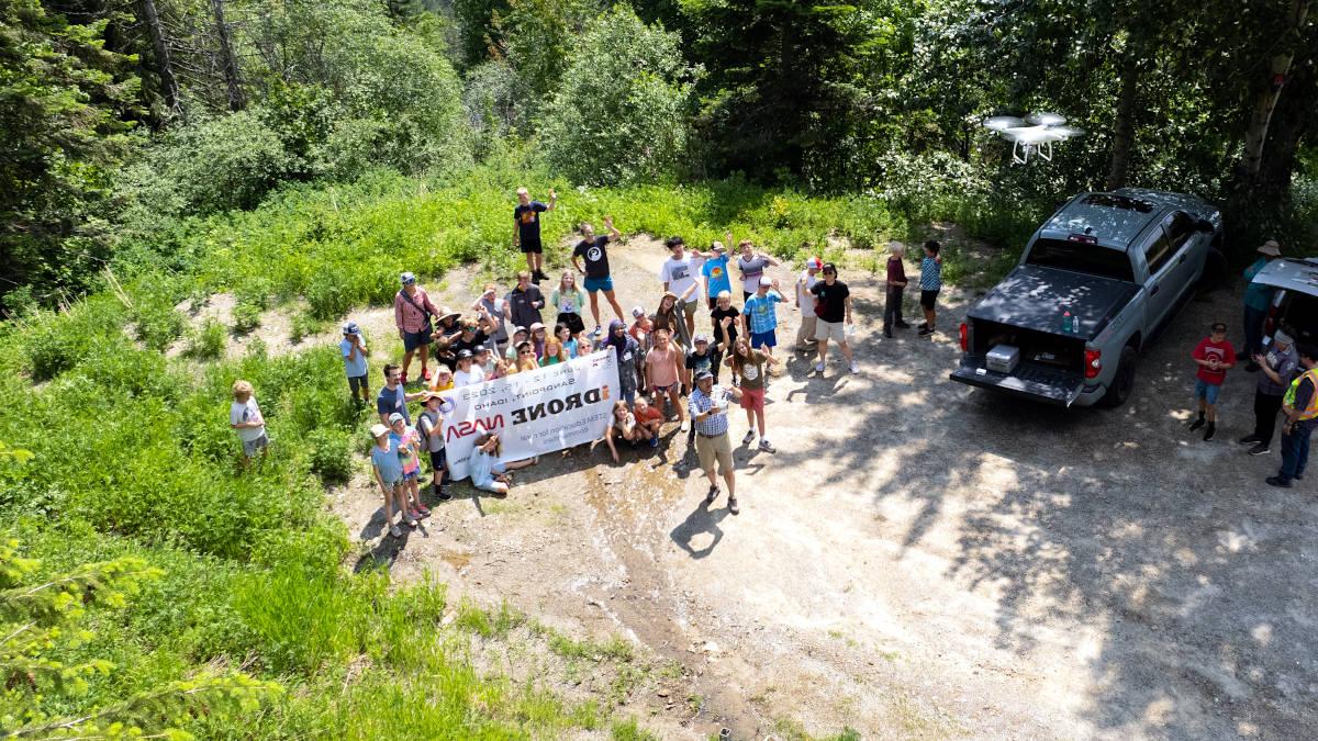 Drone photo of group standing on the ground holding a banner.