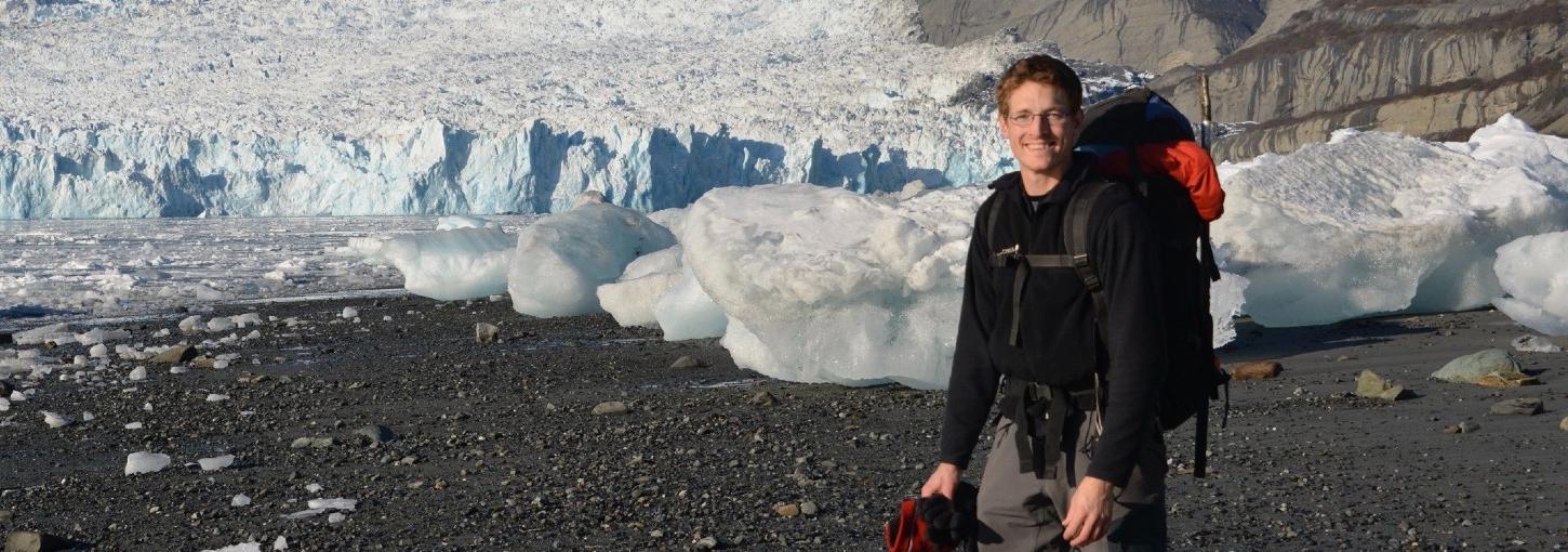 Tim Bartholomaus wears cold weather gear in front of a glacier.